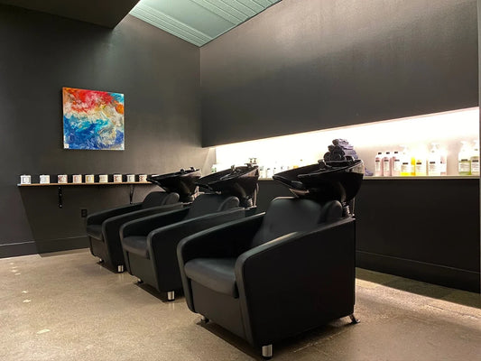 Black shampoo basins and a lit professional product shelf at Whistle & Sway Salon Company in Fort Worth