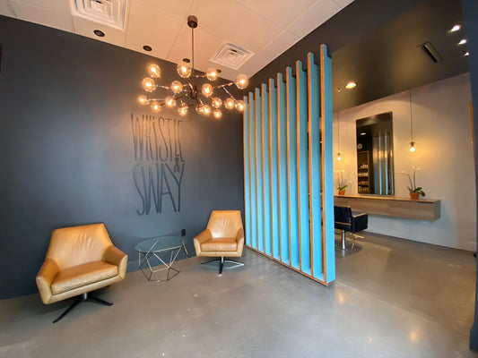 The front of Whistle & Sway Salon Company in Fort Worth with leather chairs, brass chandelier, turquoise slat wall and the retail shelf beyond