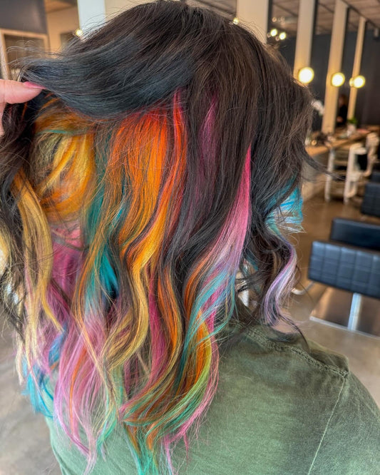 Rainbow vivid color placed as underlights beneath dark hair, orange, pink, teal and yellow, at Whistle & Sway Salon Company in Fort Worth